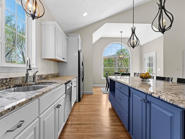 kitchen featuring blue cabinets, appliances with stainless steel finishes, vaulted ceiling, a sink, and white cabinetry