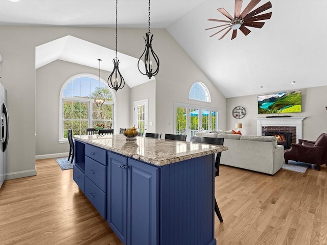 kitchen with blue cabinets, a kitchen bar, a brick fireplace, high vaulted ceiling, and light wood-style flooring