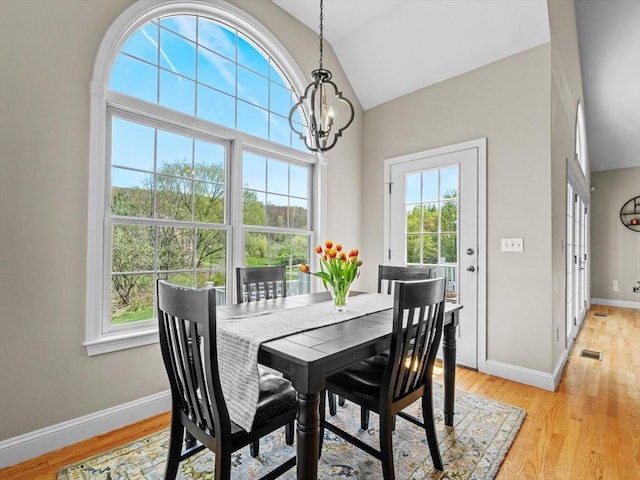 dining space with plenty of natural light, light wood finished floors, lofted ceiling, and a notable chandelier