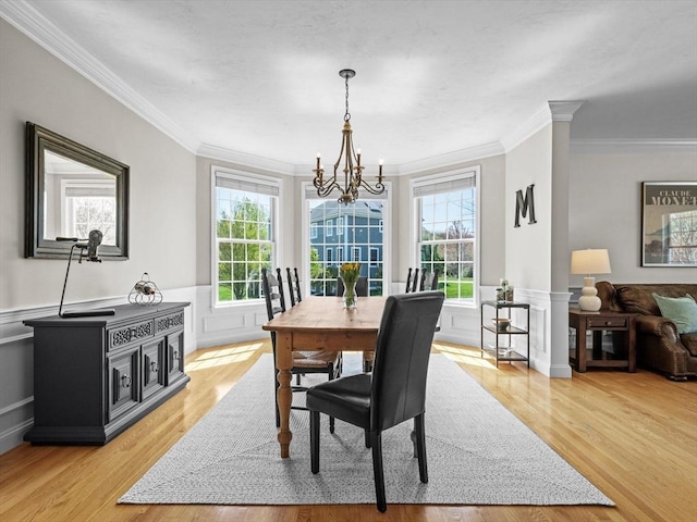 dining area with an inviting chandelier, light wood finished floors, crown molding, and wainscoting
