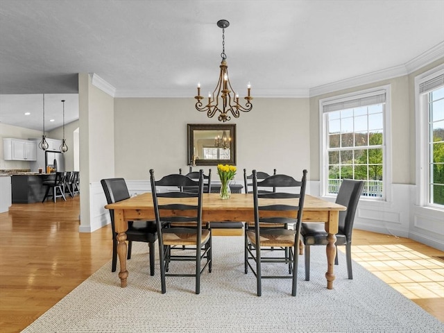 dining room featuring crown molding, light wood-style flooring, wainscoting, and a chandelier