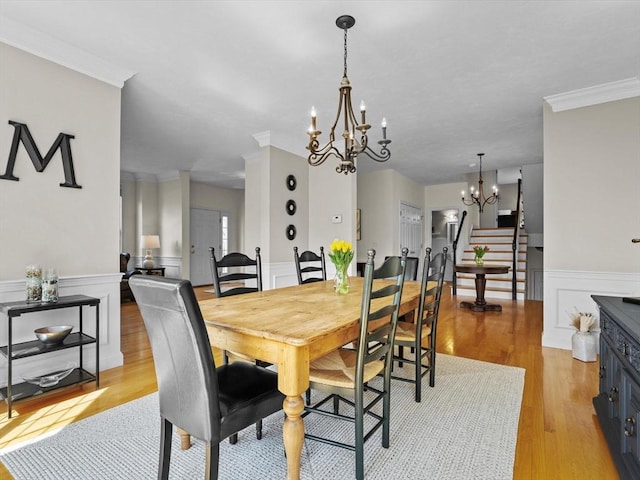dining area featuring wainscoting, light wood finished floors, an inviting chandelier, ornamental molding, and stairs
