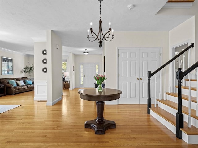 entryway with crown molding, stairs, light wood-style flooring, and a notable chandelier