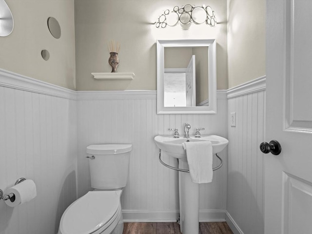 half bath with a sink, a wainscoted wall, toilet, and wood finished floors