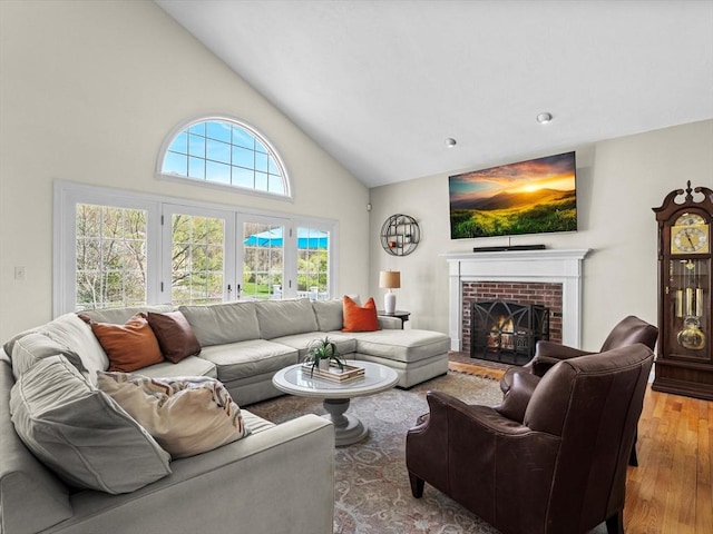 living area featuring high vaulted ceiling, a brick fireplace, and wood finished floors