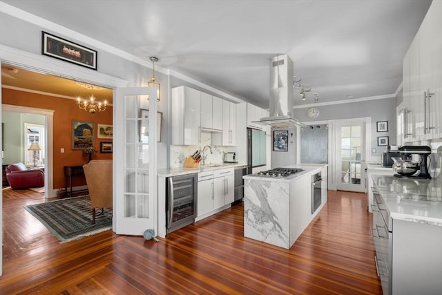 kitchen featuring white cabinets, wine cooler, appliances with stainless steel finishes, decorative light fixtures, and island exhaust hood