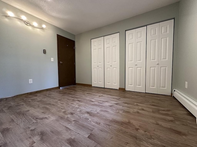 82 S Maple St Unit 44, Westfield, MA 01085 - unfurnished bedroom featuring two closets, wood finished floors, a textured ceiling, and baseboard heating