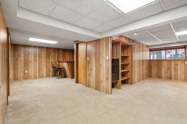 interior space featuring light carpet, a drop ceiling, and wood walls