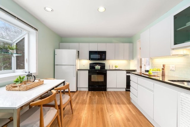 kitchen featuring backsplash, white cabinets, light wood-type flooring, and black appliances