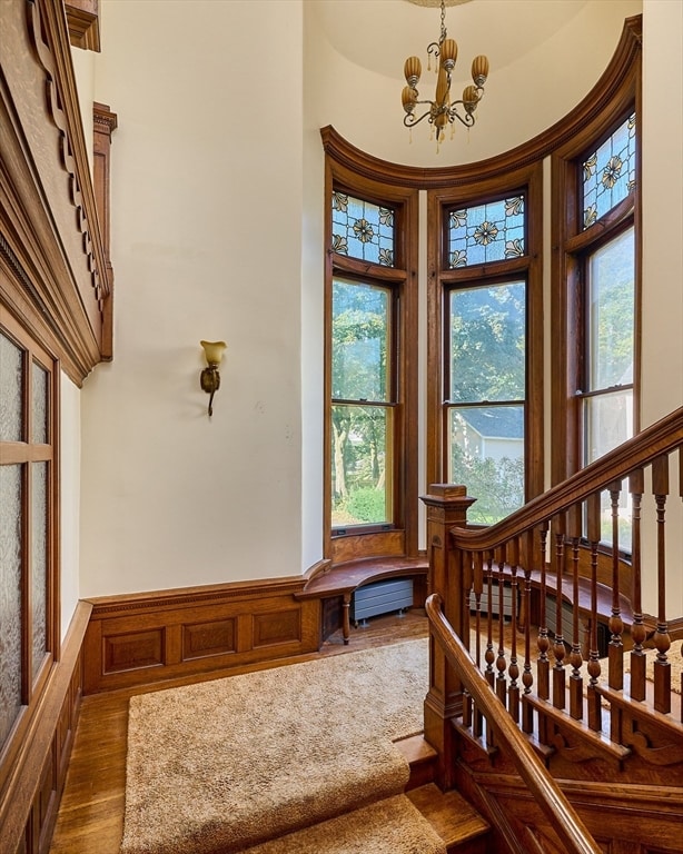 staircase with hardwood / wood-style floors, a towering ceiling, and an inviting chandelier