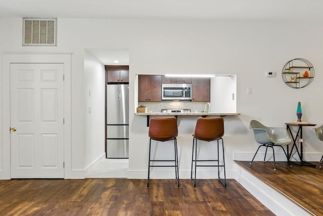 35 Nonantum St Unit E, Boston, MA 02135 - kitchen with stainless steel appliances, a kitchen breakfast bar, tasteful backsplash, a peninsula, and wood finished floors