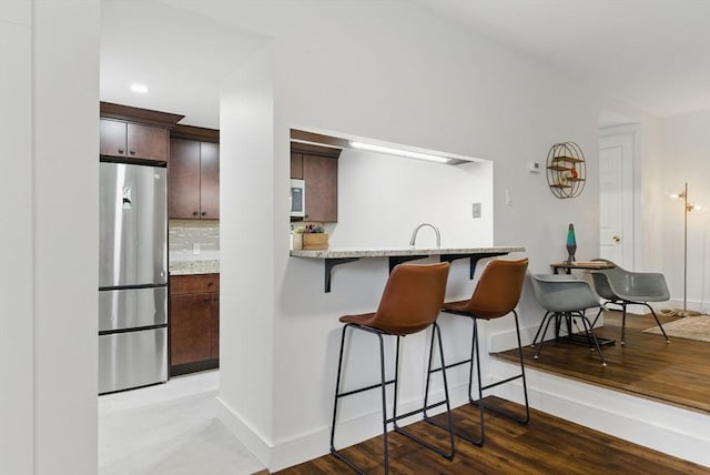 35 Nonantum St Unit E, Boston, MA 02135 - kitchen with freestanding refrigerator, a kitchen breakfast bar, decorative backsplash, baseboards, and dark brown cabinetry