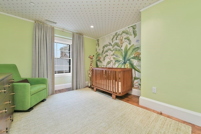 bedroom featuring crown molding, light wood-type flooring, and a nursery area