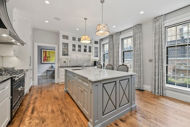 kitchen with light hardwood / wood-style floors, a center island, tasteful backsplash, wall chimney range hood, and range with two ovens