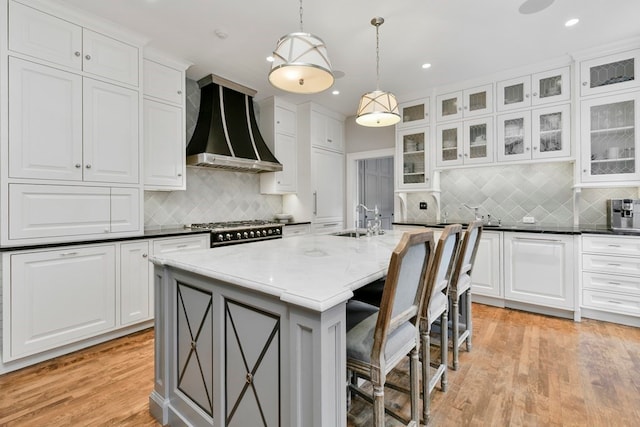 kitchen with a center island with sink, light hardwood / wood-style flooring, wall chimney exhaust hood, white cabinets, and backsplash