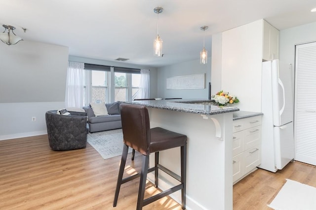 130 Tudor St Unit D, Boston, MA 02127 - kitchen featuring freestanding refrigerator, white cabinets, a breakfast bar area, and light wood finished floors