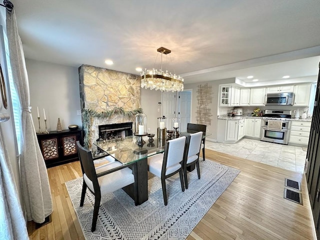 dining space with light wood-type flooring, an inviting chandelier, a stone fireplace, and visible vents