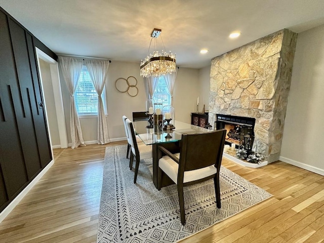 dining room featuring a stone fireplace, light wood-style floors, baseboards, and a chandelier