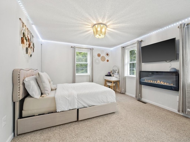 bedroom featuring multiple windows, carpet floors, baseboards, and a glass covered fireplace