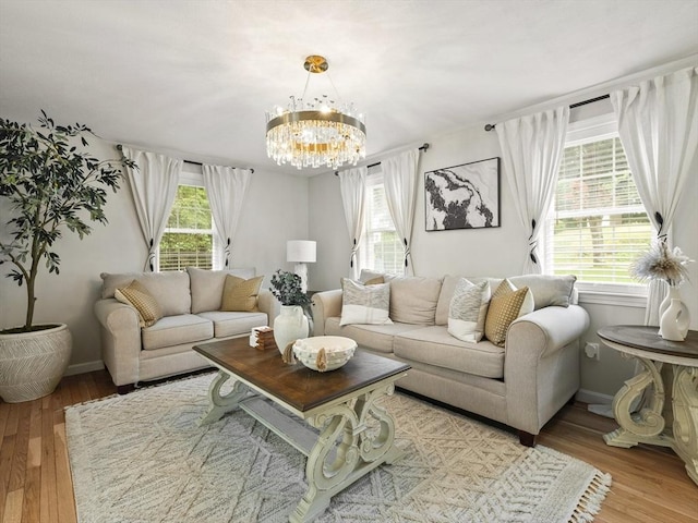 living area with baseboards, light wood-type flooring, plenty of natural light, and an inviting chandelier