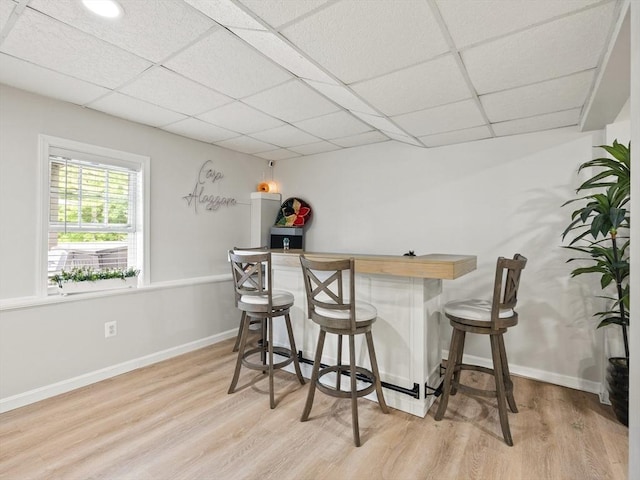 bar featuring a drop ceiling, baseboards, a bar, and light wood-style flooring