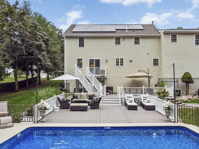 rear view of house with roof mounted solar panels, a fenced in pool, an outdoor hangout area, and a wooden deck