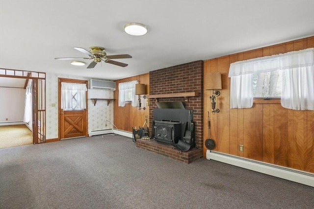 unfurnished living room with carpet floors, a baseboard heating unit, a wood stove, ceiling fan, and a wall mounted air conditioner