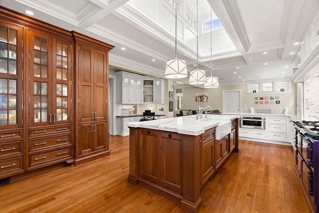 4 Cobb Ave, Manchester, MA 01944 - kitchen featuring dark wood finished floors, a large island with sink, brown cabinets, glass insert cabinets, and pendant lighting