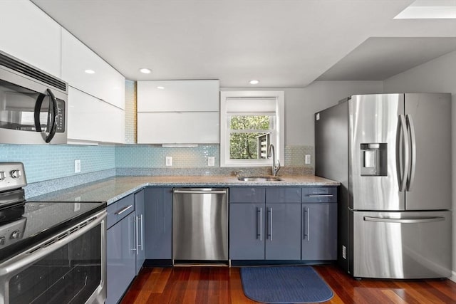 kitchen with stainless steel appliances, a sink, dark wood-type flooring, backsplash, and light stone counters
