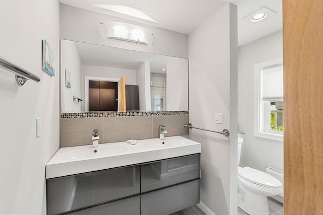 bathroom featuring toilet, double vanity, tile patterned floors, decorative backsplash, and baseboards
