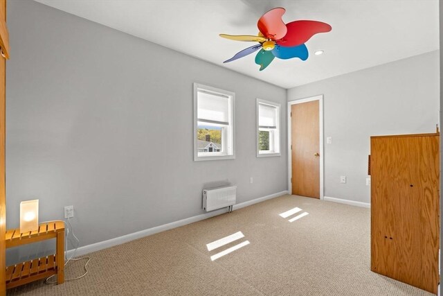 unfurnished bedroom with carpet floors, baseboards, radiator, and ceiling fan