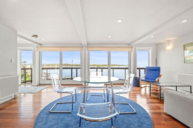 dining space featuring beam ceiling, hardwood / wood-style floors, radiator, a water view, and recessed lighting