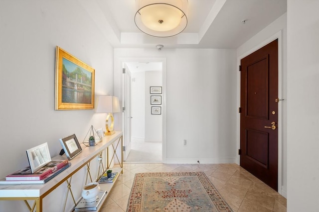 corridor with light tile patterned floors and a tray ceiling