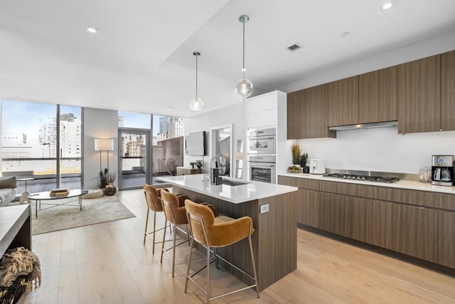 kitchen featuring pendant lighting, an island with sink, sink, light wood-type flooring, and a kitchen bar