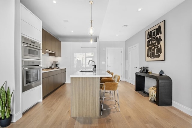 kitchen featuring pendant lighting, sink, a kitchen island with sink, white cabinetry, and light hardwood / wood-style floors