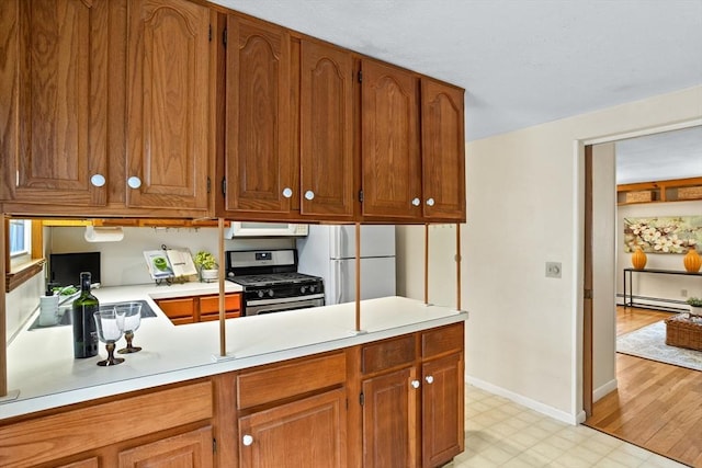 kitchen with stainless steel range with gas cooktop, kitchen peninsula, baseboard heating, and white refrigerator