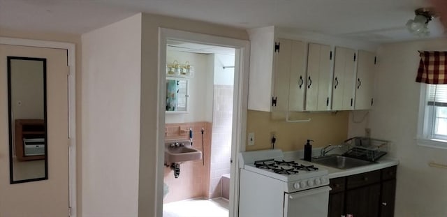 kitchen with white cabinetry, sink, tile walls, and gas range gas stove