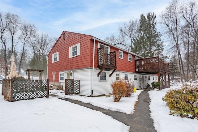 snow covered rear of property with a deck and a pergola