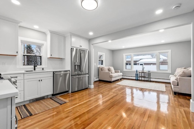 kitchen featuring baseboard heating, white cabinets, stainless steel appliances, sink, and light hardwood / wood-style flooring