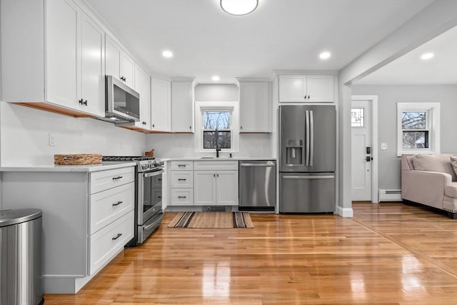 kitchen with stainless steel appliances, white cabinetry, light hardwood / wood-style flooring, and baseboard heating