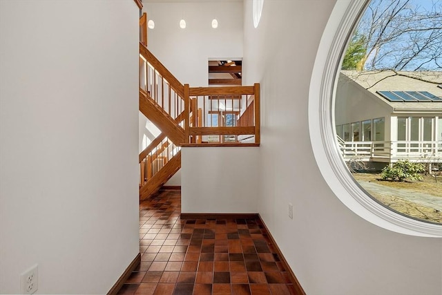 hallway with baseboards, a towering ceiling, tile patterned floors, and stairway