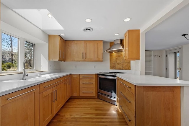 kitchen featuring a sink, light wood finished floors, stainless steel range with electric stovetop, a peninsula, and wall chimney range hood