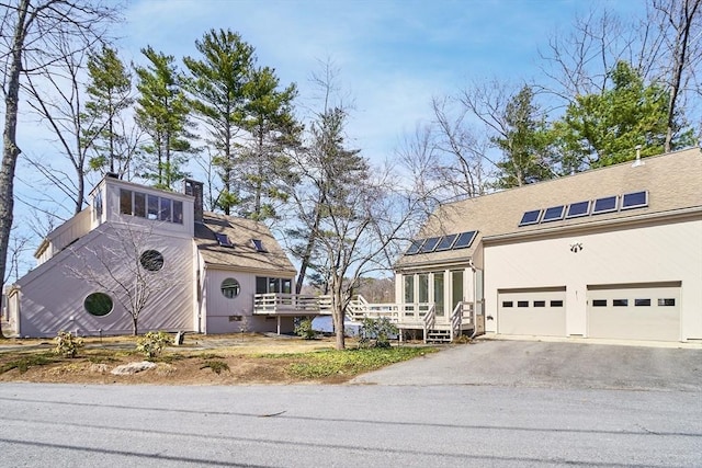 view of front of property featuring roof mounted solar panels, a chimney, stucco siding, a deck, and driveway