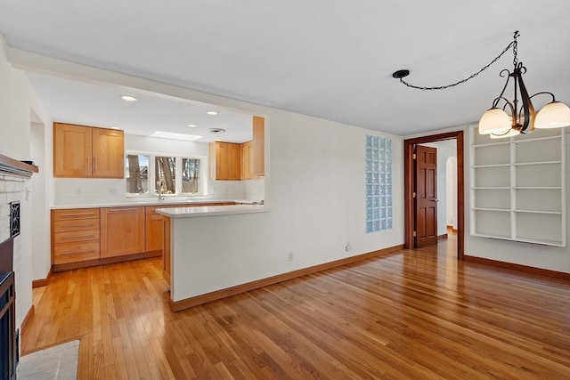 kitchen with baseboards, light countertops, light wood-style floors, and a fireplace