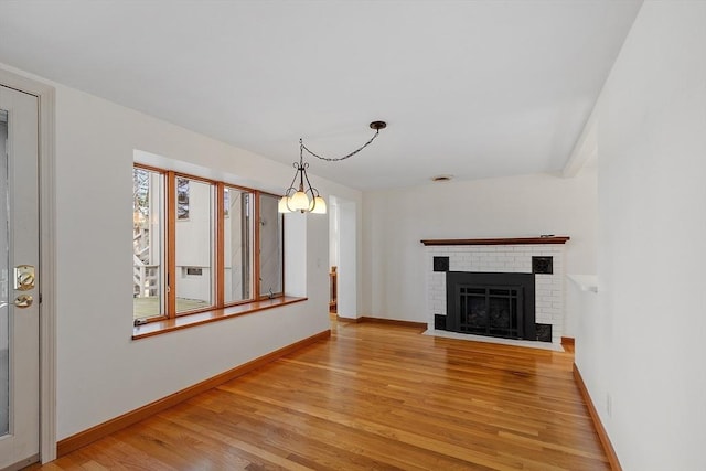 unfurnished living room with baseboards, light wood-type flooring, and a brick fireplace