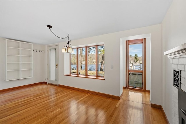 unfurnished dining area with baseboards, a fireplace, a chandelier, and light wood finished floors