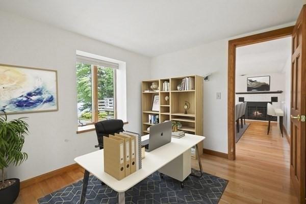 office space featuring baseboards, a warm lit fireplace, and light wood-style flooring