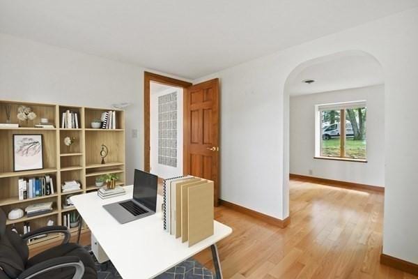 office area with baseboards, arched walkways, and light wood-style flooring