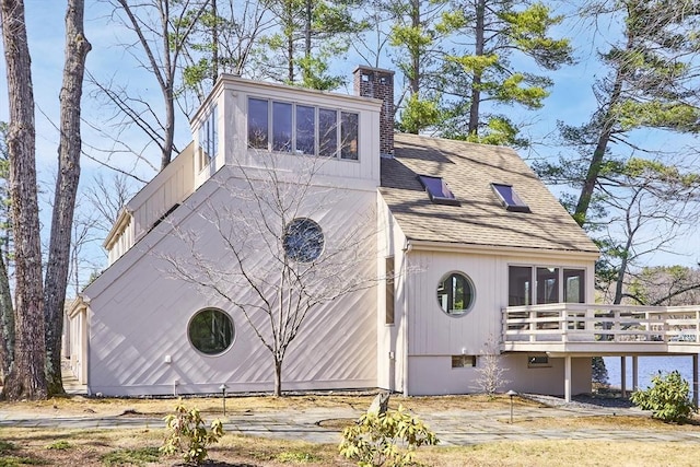 exterior space with a chimney, a shingled roof, and a deck