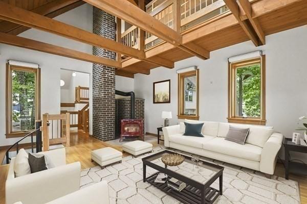 living room with wood finished floors, a wood stove, beamed ceiling, and plenty of natural light